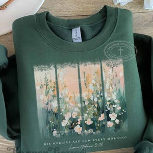 May include: A dark green sweatshirt with a floral design and the text "HIS MERCIES ARE NEW EVERY MORNING Lamentations 3:23".