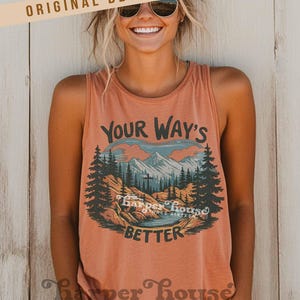 May include: A coral-colored tank top with a graphic design featuring a mountain landscape, trees, and the text "Your Way's Better." The tank top has a scoop neck and is sleeveless. The brand name "Harper House Three Sixteen" is printed at the bottom.