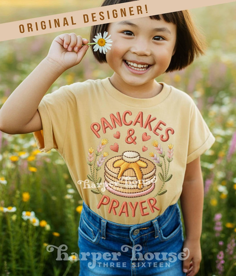 May include: A child wearing a mustard yellow t-shirt with the embroidered text "PANCAKES & PRAYER" and a stack of pancakes. The child is smiling and holding a daisy. The shirt also has the text "Harper House THREE SIXTEEN".