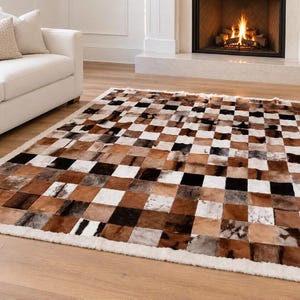 May include: A rectangular area rug featuring a patchwork design of square panels in varying shades of brown, black, and white. The rug is constructed from individual pieces of animal hide with a visible fur texture and a solid white border.