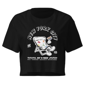 May include: A black cropped t-shirt featuring a graphic of a cartoon pizza slice sitting in a beach chair, holding a rainbow flag. The text reads NEW YORK CITY, 25C SLICES, MADE FRESH, HOT N FRESH, LOCAL, HOMEMADE, DESIGNED BY @MEGANLACDESIGNS.