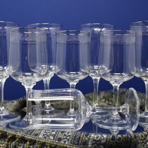 May include: A collection of clear glass wine glasses with a decorative rim. One glass is lying on its side in front of the others. The glasses are arranged on a patterned surface against a blue background.