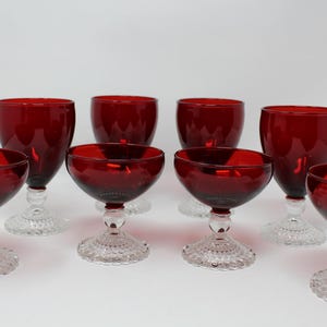 May include: Set of eight red glass stemmed goblets with clear, textured bases. The goblets are in various sizes and shapes.