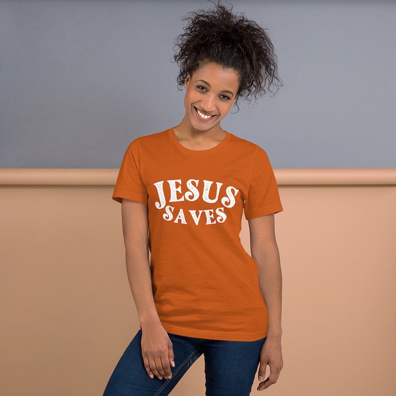 Pu&ograve; includere: Una donna indossa una maglietta arancione con la scritta "JESUS SAVES" in lettere bianche.