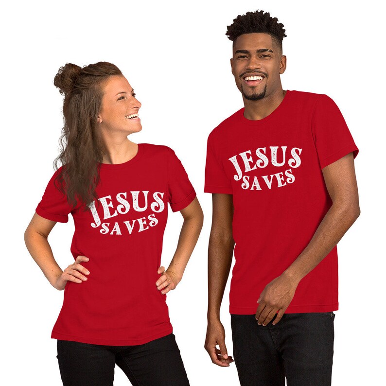 Pu&ograve; includere: Due persone indossano magliette rosse con il testo "JESUS SAVES" in bianco. Il testo &egrave; in un font in stile vintage.