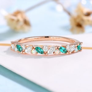 Puede incluir: Anillo de oro rosa con esmeraldas y piedras blancas talladas en marquesa alternadas. La banda del anillo es de oro rosa delicado, y las piedras están engastadas en un patrón repetitivo. Es una pieza de joyería.