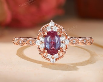 Può includere: Un anello in oro rosa con una pietra centrale di taglio ovale color rosso porpora circondata da un alone di piccole pietre bianche rotonde. La montatura presenta una cornice in filigrana e la fascia mostra un motivo smerlato con pietre.
