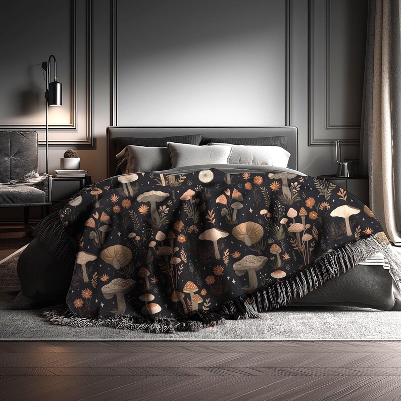 May include: A black throw blanket with a repeating pattern of mushrooms, flowers, and foliage in shades of tan, orange, and white. The blanket has a fringed edge and is draped over a bed. The overall theme is nature and botanical.