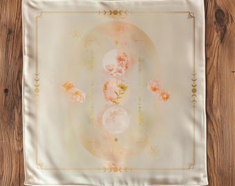 Op de afbeelding: Een witte vierkante stof met een gouden rand en een ontwerp van een cirkel met manen en bloemen in roze en gouden tinten.
