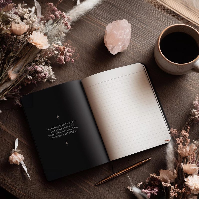 May include: An open black notebook with lined pages, a gold pen, and a cup of coffee on a wooden surface. A pink crystal and dried flowers are also present. The text on the left page reads: "The journey inward is a path to integration, where the terrain of the void is dark but the insight is full of light."