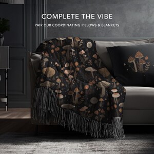 May include: A black throw blanket with a mushroom pattern and fringe is draped over a sofa. A matching pillow with a mushroom design is also on the sofa. The text "COMPLETE THE VIBE" and "PAIR OUR COORDINATING PILLOWS & BLANKETS" is visible.