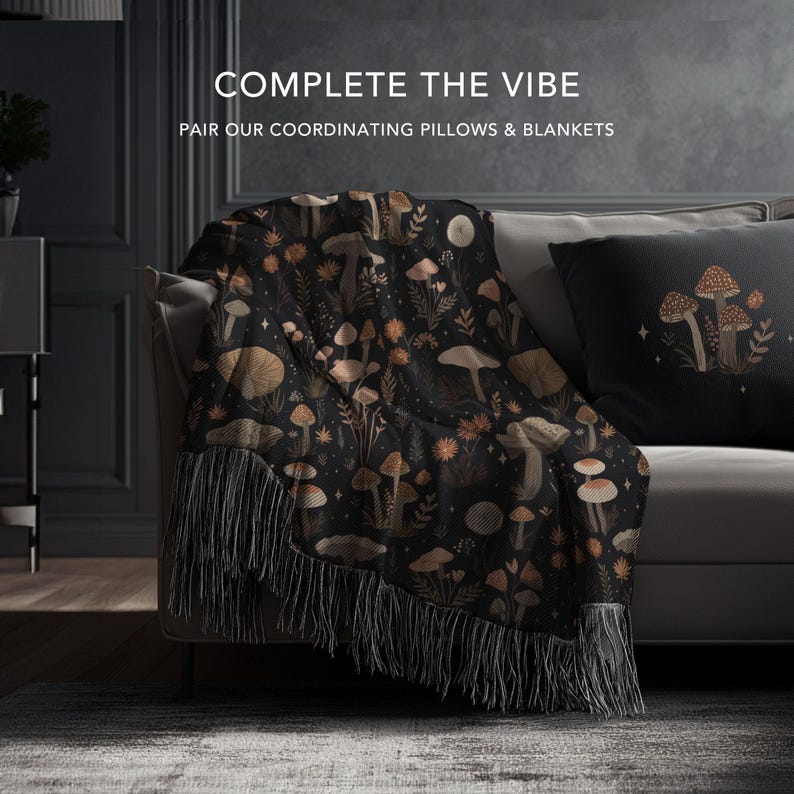 May include: A black throw blanket with a mushroom pattern and fringe is draped over a sofa. A matching pillow with a mushroom design is also on the sofa. The text "COMPLETE THE VIBE" and "PAIR OUR COORDINATING PILLOWS & BLANKETS" is visible.