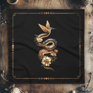 May include: A black square fabric with a gold frame and a design of a snake with a hummingbird on its back. The snake is surrounded by flowers and leaves. The design is on a black background.