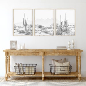 Puede incluir: Una consola de madera con dos cestas de alambre negro, una con libros y la otra con almohadas. La mesa est&aacute; decorada con velas y una peque&ntilde;a impresi&oacute;n enmarcada. Tres impresiones enmarcadas en blanco y negro de paisajes des&eacute;rticos con cactus cuelgan de la pared sobre la mesa.