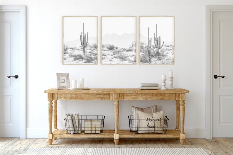 Puede incluir: Una consola de madera con dos cestas de alambre negro, una con libros y la otra con almohadas. La mesa est&aacute; decorada con velas y una peque&ntilde;a impresi&oacute;n enmarcada. Tres impresiones enmarcadas en blanco y negro de paisajes des&eacute;rticos con cactus cuelgan de la pared sobre la mesa.