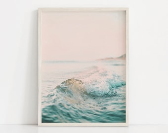 May include: A close-up of a wave crashing on a beach with a soft pink and blue color palette.