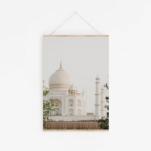 May include: A white marble building with a large dome and minarets, known as the Taj Mahal, is pictured against a light blue sky. The building is surrounded by a green lawn and trees.