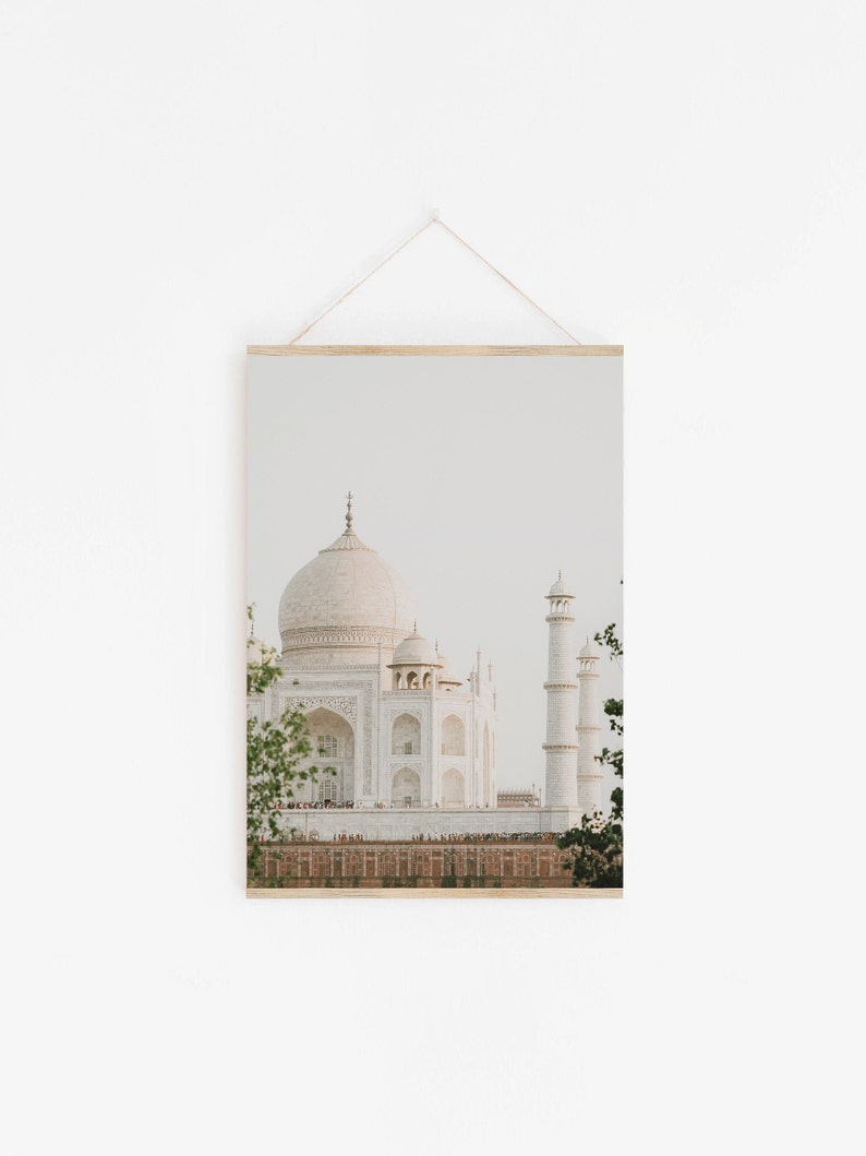 May include: A white marble building with a large dome and minarets, known as the Taj Mahal, is pictured against a light blue sky. The building is surrounded by a green lawn and trees.