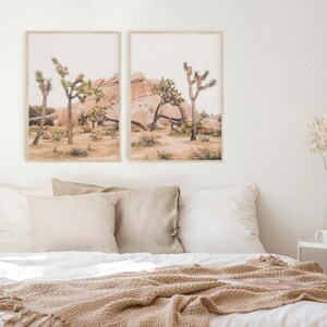 K&ouml;nnte beinhalten: Zwei gerahmte Drucke einer W&uuml;stenlandschaft mit Joshua-B&auml;umen und gro&szlig;en Felsen. Die Drucke h&auml;ngen an einer wei&szlig;en Wand &uuml;ber einem Bett mit einer beigefarbenen Decke.
