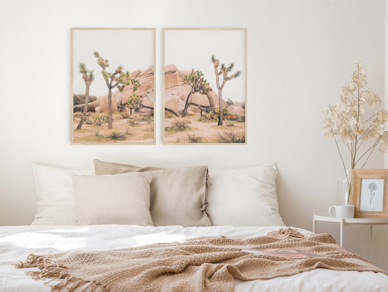 K&ouml;nnte beinhalten: Zwei gerahmte Drucke einer W&uuml;stenlandschaft mit Joshua-B&auml;umen und gro&szlig;en Felsen. Die Drucke h&auml;ngen an einer wei&szlig;en Wand &uuml;ber einem Bett mit einer beigefarbenen Decke.