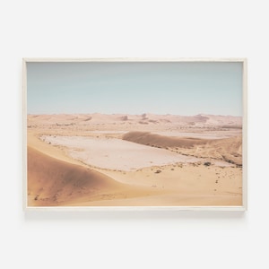 May include: A panoramic view of a desert landscape with sand dunes and a dry lake bed. The sky is a pale blue, and the sand is a warm beige color.
