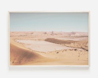 May include: A panoramic view of a desert landscape with sand dunes and a dry lake bed. The sky is a pale blue, and the sand is a warm beige color.