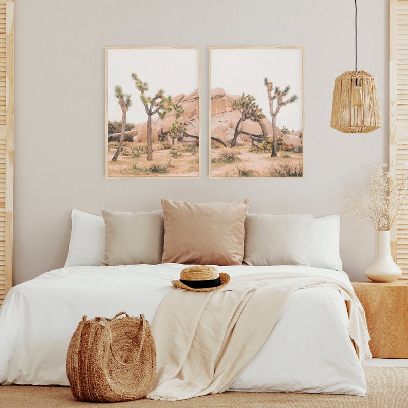 K&ouml;nnte beinhalten: Zwei gerahmte Drucke des Joshua-Tree-Nationalparks in Kalifornien. Die Drucke zeigen eine gro&szlig;e Felsformation und Joshua-Trees. Die Drucke h&auml;ngen an einer hellgrauen Wand &uuml;ber einem wei&szlig;en Bett mit einer braunen Decke und einem Strohhut.