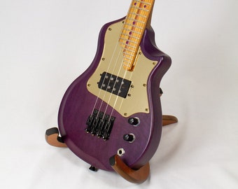 May include: A purple electric guitar with a gold pickguard and a wooden stand. The guitar has a unique shape and a single pickup.
