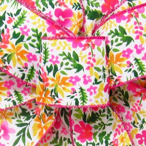May include: White ribbon with a pink, orange, and green floral print. The ribbon has a pink edge.