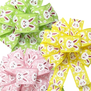 May include: Three Easter bunny-themed bows in pink, green, and yellow. Each bow features a white bunny face with pink ears and glitter accents on a white background with pink, green, or yellow polka dots.