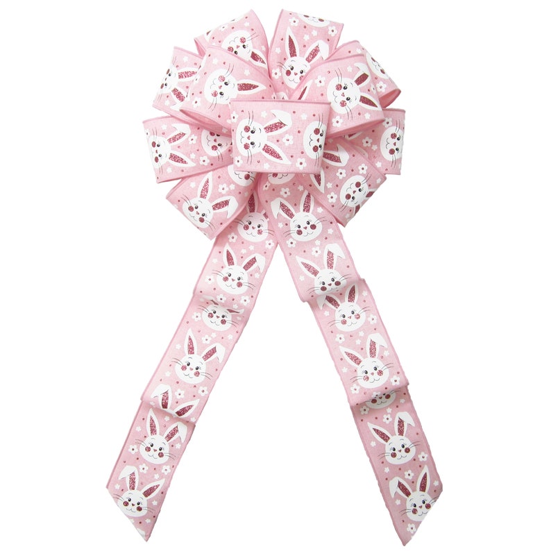 May include: Pink bow with white bunny faces and pink glitter. The bow is made of ribbon and has a loop in the center. The tails of the bow are long and flowing.
