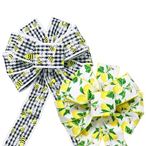 May include: Two decorative bows made of ribbon. One bow is black and white gingham with a bee pattern. The other bow is white with a lemon and bee pattern.