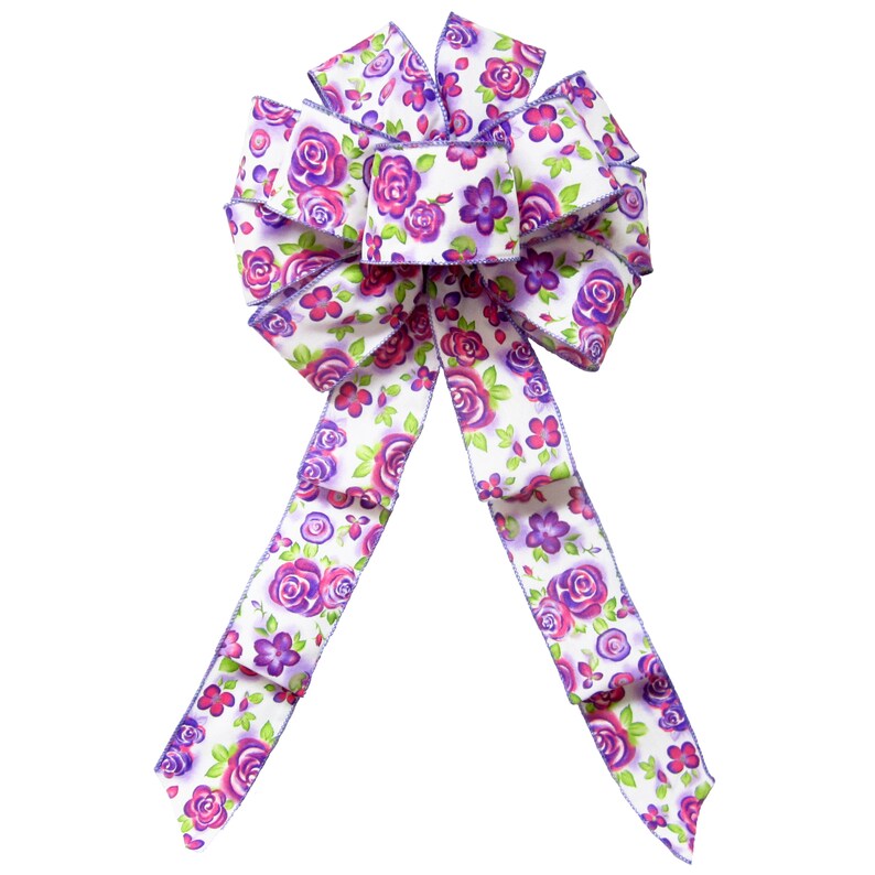 May include: A white bow with purple and pink floral print. The bow is made of satin ribbon and has a wired edge.