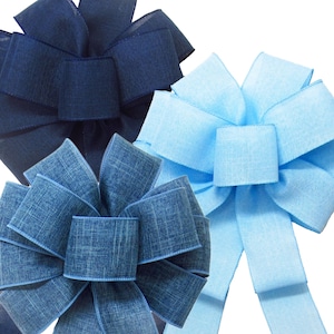 May include: Three large fabric bows in shades of blue. The bows are made of a textured, woven fabric. The bow on the left is a dark navy blue, the bow in the center is a light blue denim, and the bow on the right is a light sky blue.