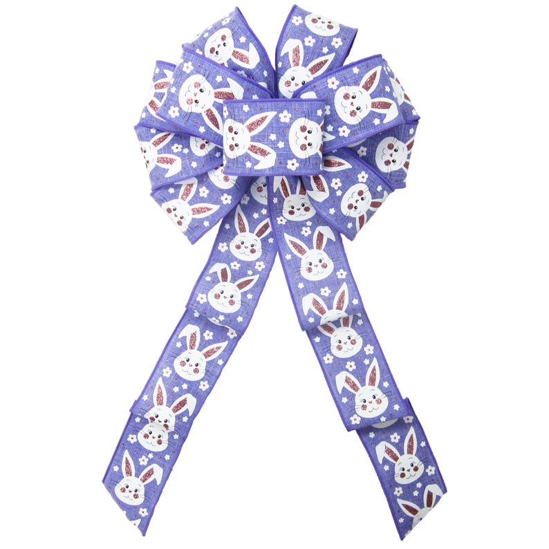 May include: A purple Easter bow with a repeating pattern of white bunny faces and small white flowers. The bow has long tails, ideal for spring decorations. The ribbon is made of a textured material.