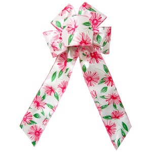 May include: A white satin ribbon bow with a pink floral print. The bow is tied with a loop and tails. The ribbon has a green leaf pattern.