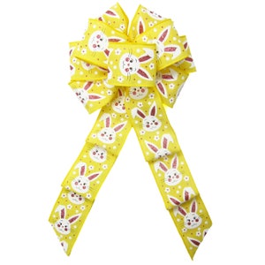 May include: A yellow bow with a white bunny rabbit pattern and pink accents. The bow is made of a glittery fabric and is perfect for Easter decorations.