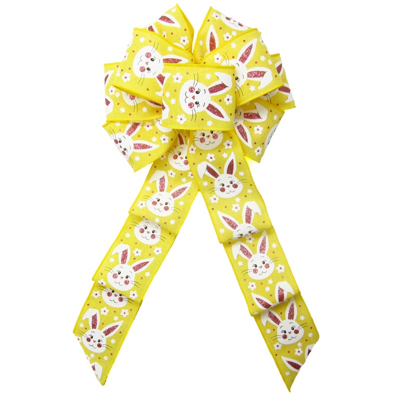 May include: A yellow bow with a white bunny rabbit pattern and pink accents. The bow is made of a glittery fabric and is perfect for Easter decorations.