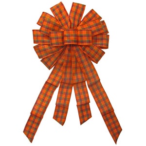 May include: A large orange and green plaid bow with multiple tails. The bow is made of a soft, woven fabric.