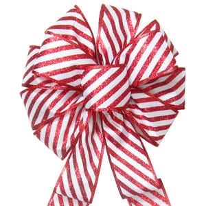 May include: A decorative bow made of ribbon featuring a pattern of diagonal red glitter stripes alternating with white stripes. The bow has a central knot and two long, hanging tails, all constructed from the same striped material.