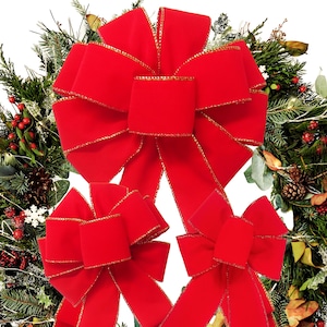 May include: Three vibrant red velvet bows with gold-trimmed edges. The large central bow is positioned above two smaller matching bows. Each bow features wide, soft fabric loops and long, flowing tails, creating a classic decorative appearance.