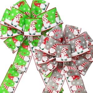 May include: Two Christmas bows with a gnome pattern. One bow is green with white snowflakes and red dots. The other bow is gray with white snowflakes and red dots.