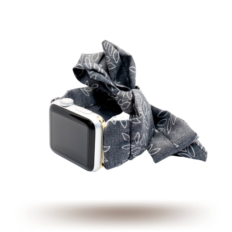 May include: A grey Apple Watch with a white and grey patterned fabric band. The band is tied in a bow.
