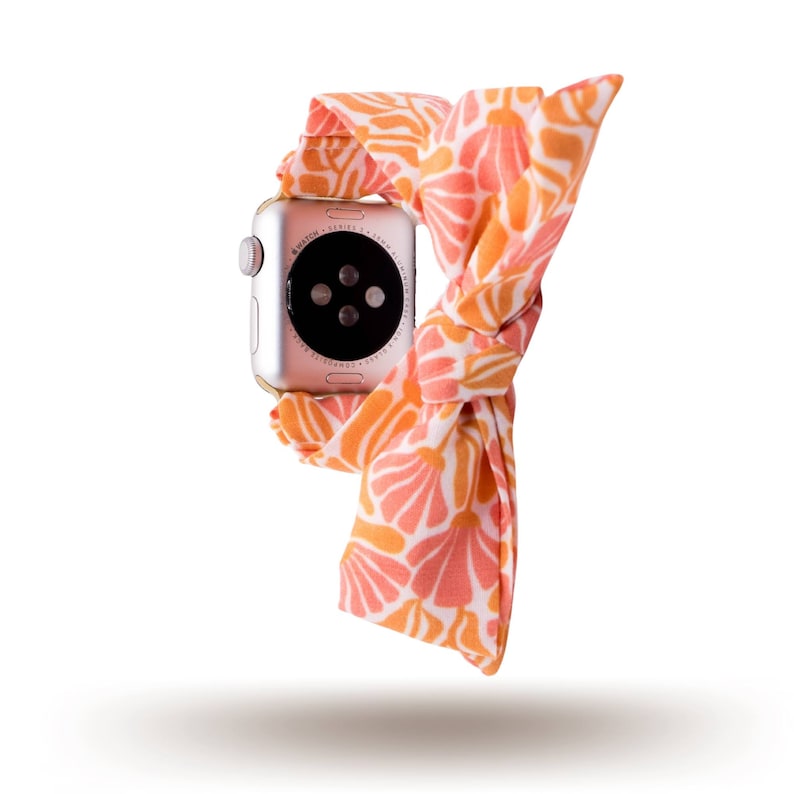 May include: A silver Apple Watch with a coral and white patterned fabric band. The watch face is black and displays the time.