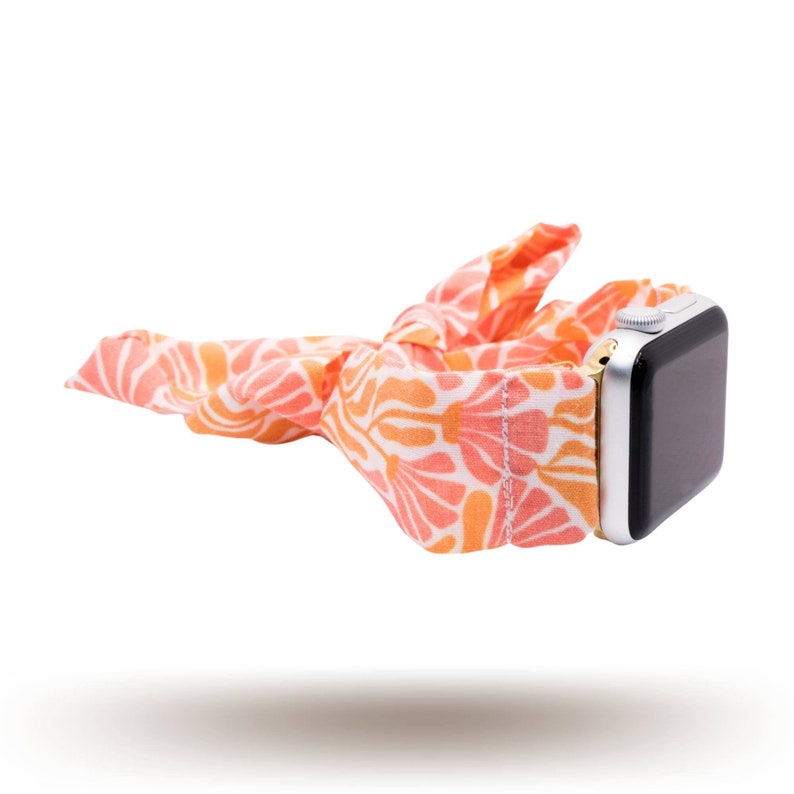 May include: A pink and orange patterned fabric watch band with a silver watch face.