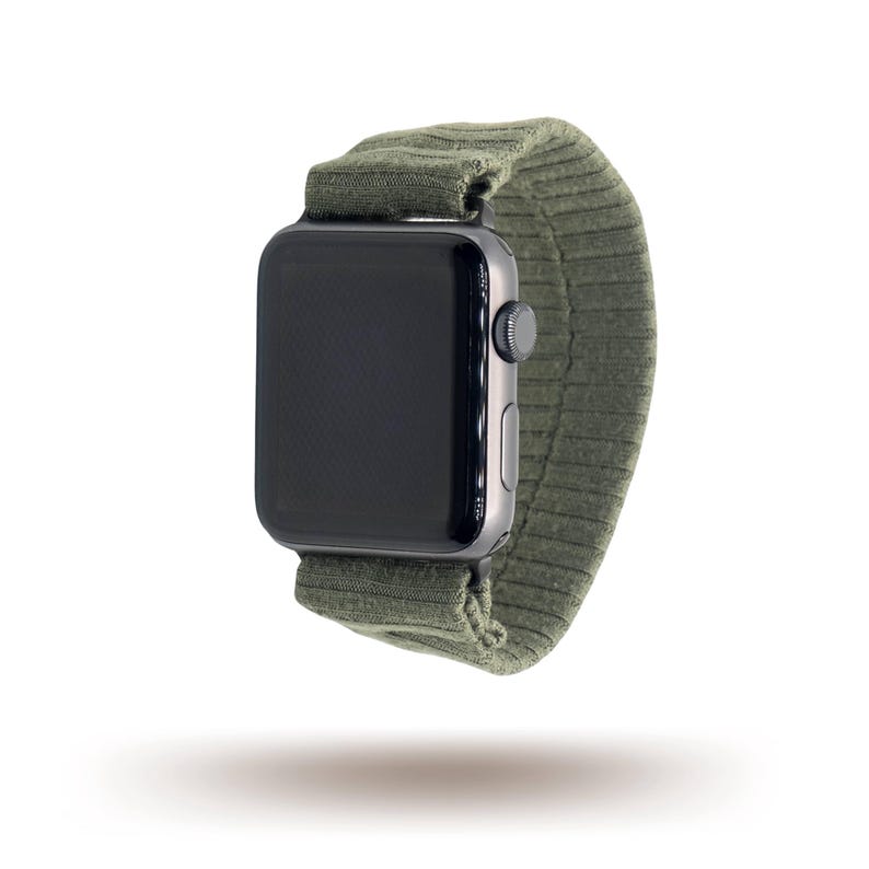 May include: A black smartwatch with a dark green ribbed fabric strap. The watch features a rectangular screen and a silver side button. The strap is made of a soft, flexible material, and the watch is suspended in the air.