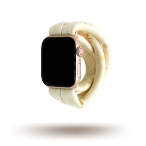May include: A gold Apple Watch with a white and gold patterned band. The watch face is black and the band is made of a soft, flexible material.