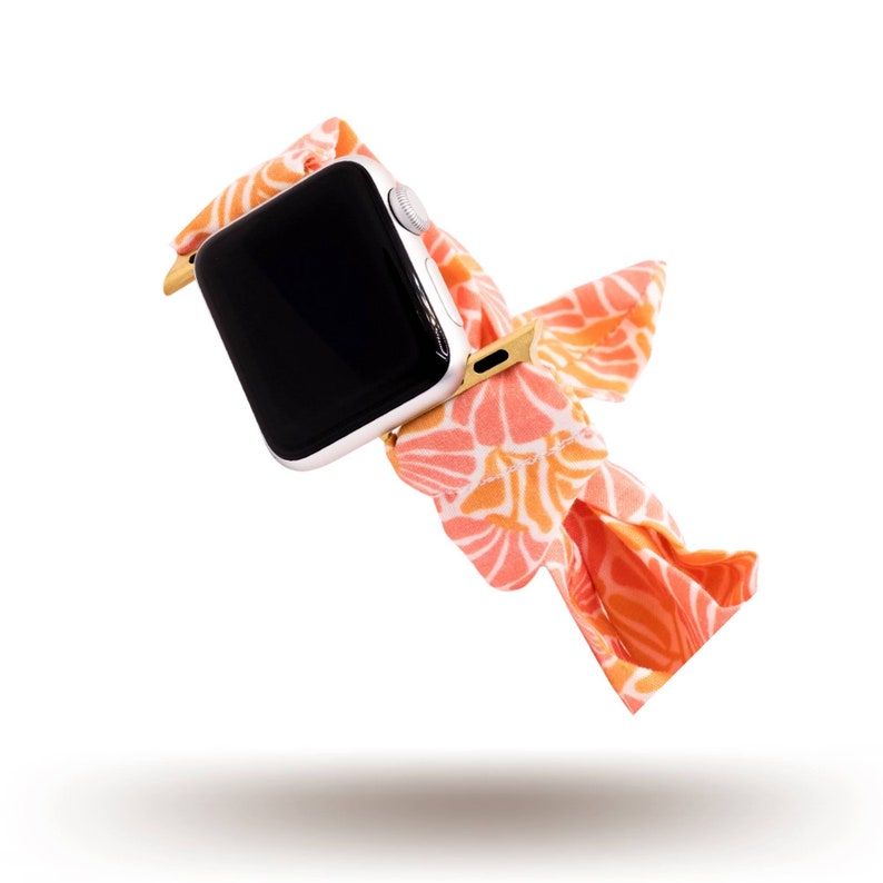 May include: A pink and orange floral patterned watch band for a smartwatch. The band is made of fabric and has a gold buckle.