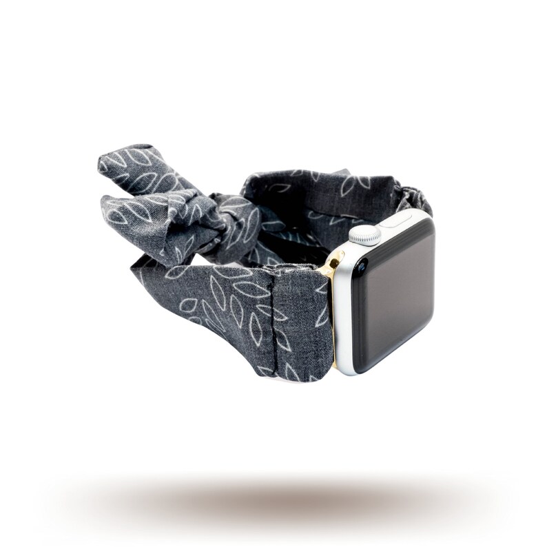 May include: A grey and white patterned fabric watch band with a gold accent and a silver Apple Watch.