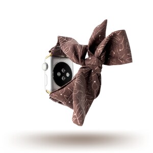 May include: A brown fabric watch strap with a floral pattern. The strap is tied in a bow and is wrapped around a silver smartwatch.